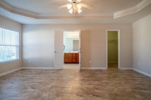 unfurnished bedroom with a textured ceiling, a walk in closet, baseboards, and ornamental molding