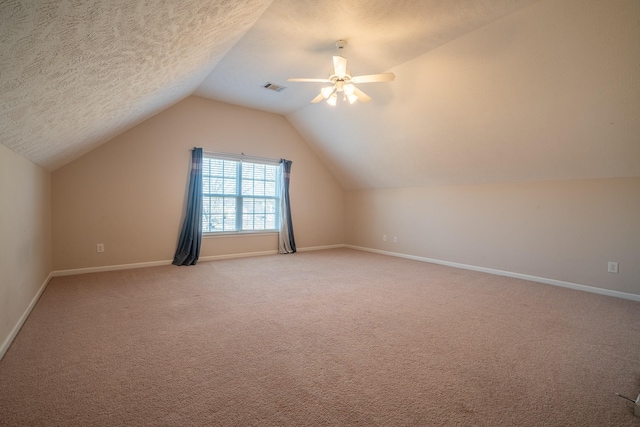 additional living space featuring a textured ceiling, a ceiling fan, visible vents, vaulted ceiling, and light carpet