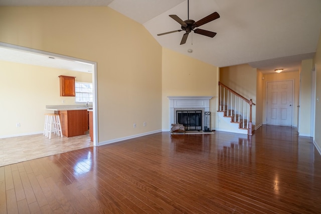 unfurnished living room with baseboards, a fireplace with raised hearth, dark wood-style flooring, and ceiling fan