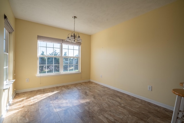 unfurnished dining area featuring a textured ceiling, baseboards, and an inviting chandelier