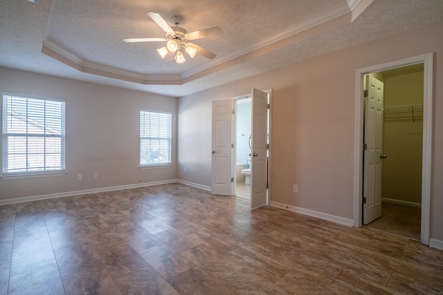 unfurnished bedroom featuring multiple windows, a textured ceiling, a tray ceiling, and ornamental molding