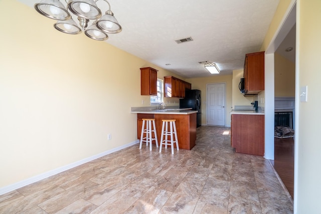 kitchen with visible vents, a kitchen breakfast bar, a peninsula, brown cabinetry, and light countertops