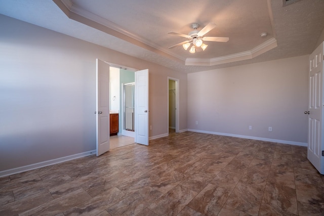 unfurnished bedroom featuring a walk in closet, ensuite bathroom, a tray ceiling, crown molding, and baseboards