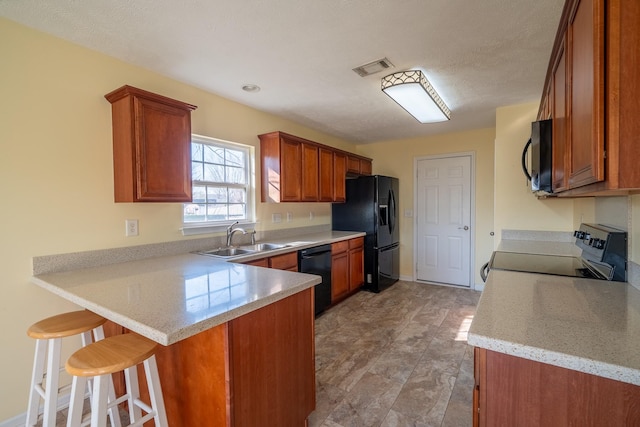 kitchen with a breakfast bar, a peninsula, brown cabinetry, black appliances, and a sink