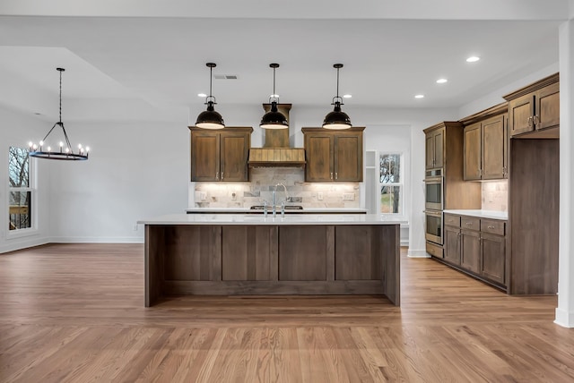 kitchen with custom range hood, a sink, stainless steel double oven, light countertops, and decorative backsplash