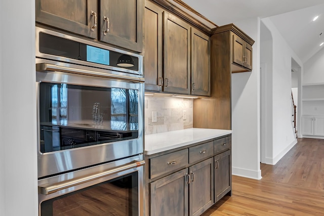 kitchen featuring baseboards, decorative backsplash, light countertops, light wood-style floors, and double oven