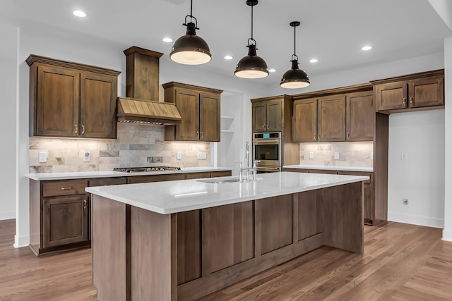 kitchen with a center island with sink, a sink, wall chimney range hood, stainless steel appliances, and light countertops