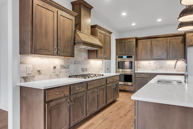 kitchen with light wood-type flooring, a sink, wall chimney range hood, appliances with stainless steel finishes, and light countertops