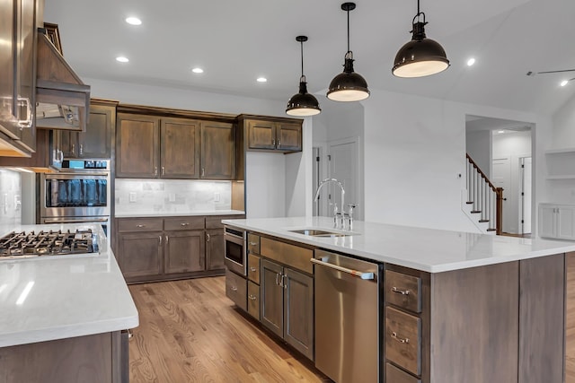 kitchen with light wood finished floors, backsplash, pendant lighting, stainless steel appliances, and a sink