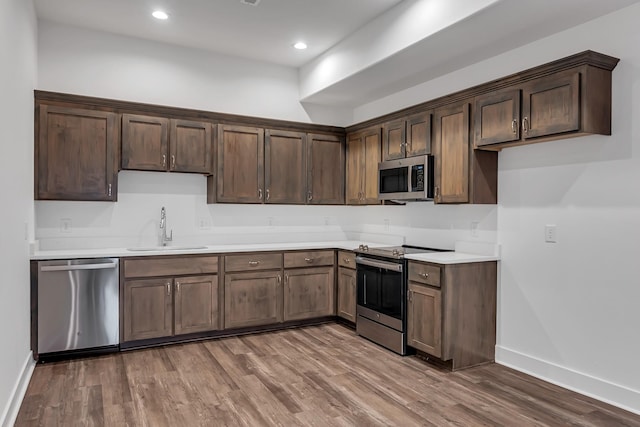 kitchen featuring wood finished floors, baseboards, a sink, light countertops, and appliances with stainless steel finishes