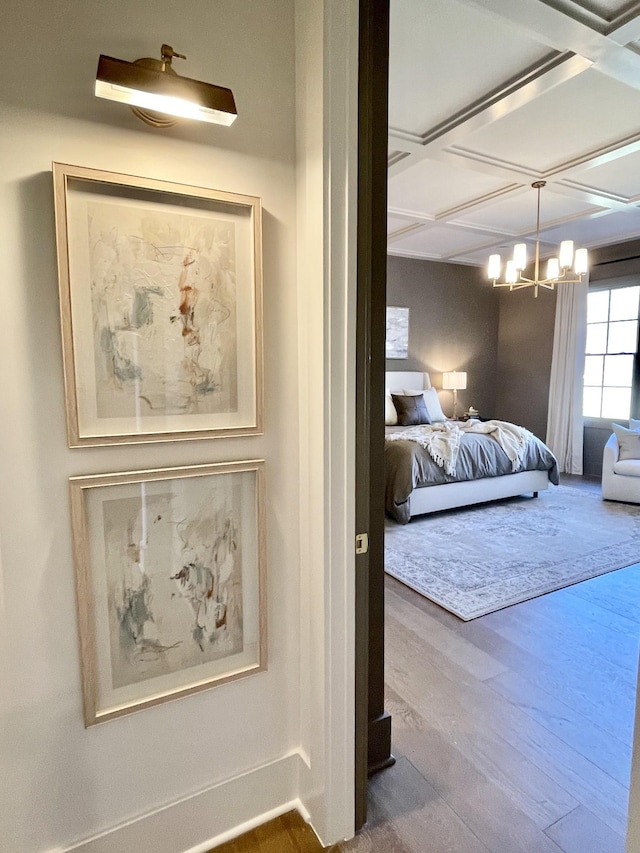 bedroom featuring a notable chandelier, coffered ceiling, and wood finished floors