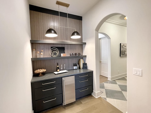 bar featuring baseboards, light wood-style flooring, arched walkways, refrigerator, and a bar