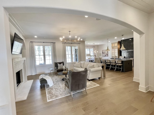 living room featuring light wood-type flooring, a high end fireplace, recessed lighting, arched walkways, and a chandelier