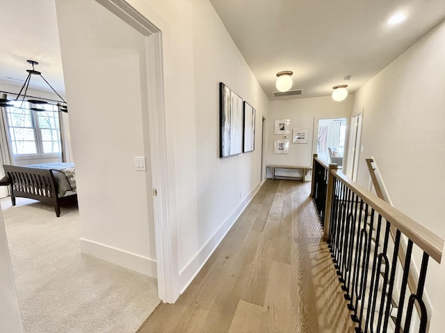 corridor featuring light wood-type flooring, an upstairs landing, visible vents, and baseboards