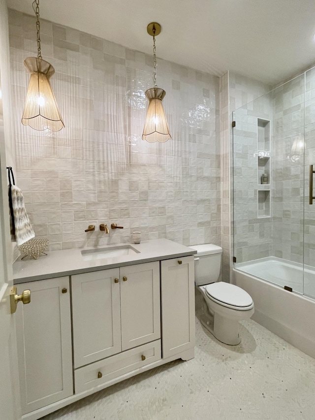 bathroom featuring combined bath / shower with glass door, toilet, tile walls, and vanity