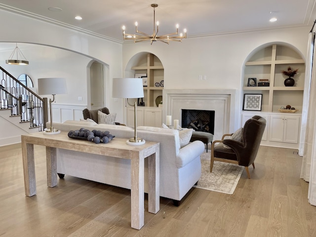 living room with built in features, wood finished floors, an inviting chandelier, and ornamental molding