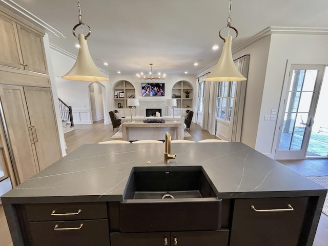 kitchen with built in shelves, a kitchen island with sink, ornamental molding, open floor plan, and a fireplace