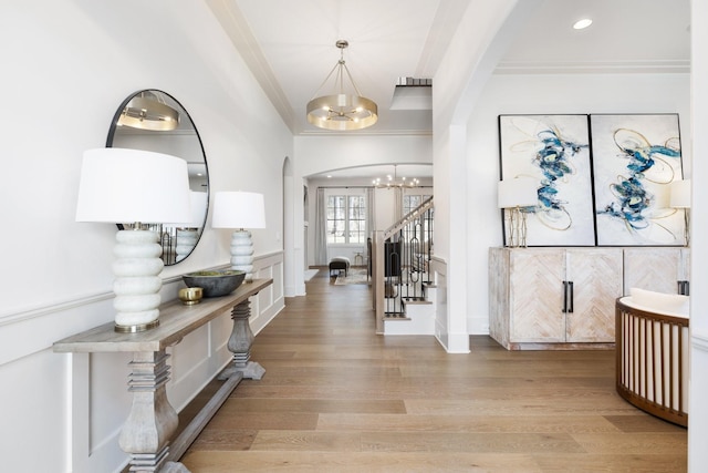 entryway featuring crown molding, stairs, light wood-type flooring, arched walkways, and a notable chandelier