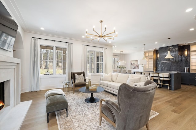 living area with light wood finished floors, recessed lighting, an inviting chandelier, a fireplace, and crown molding