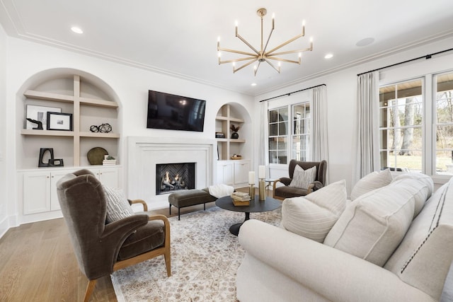 living room featuring built in shelves, light wood-style flooring, ornamental molding, recessed lighting, and a chandelier