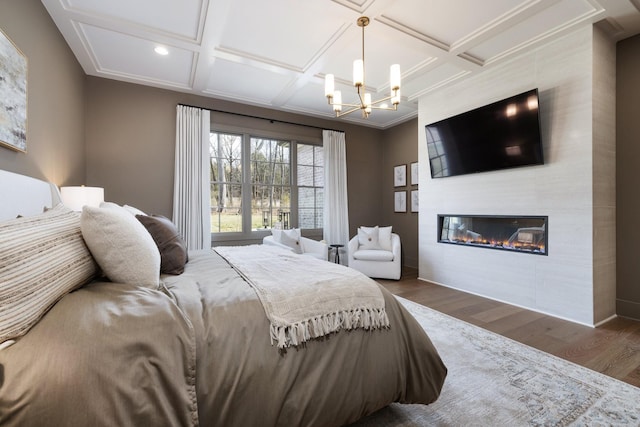 bedroom featuring beam ceiling, coffered ceiling, wood finished floors, a large fireplace, and an inviting chandelier