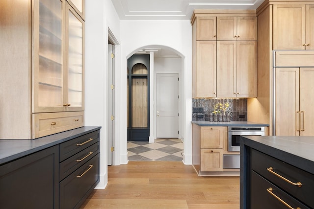 kitchen with arched walkways, light brown cabinets, paneled fridge, and stainless steel oven