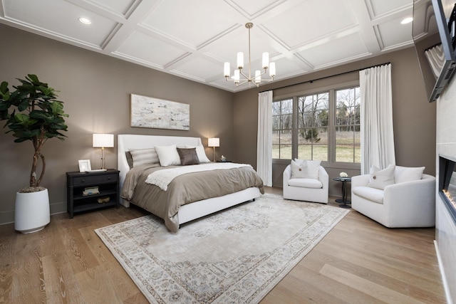 bedroom with a glass covered fireplace, light wood-style flooring, a notable chandelier, and coffered ceiling