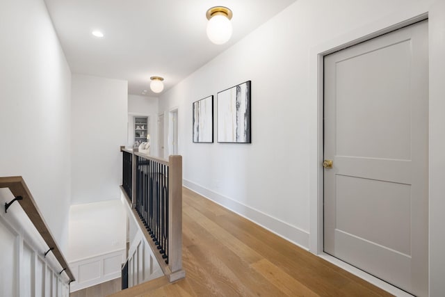 hall with an upstairs landing, baseboards, and light wood-style floors