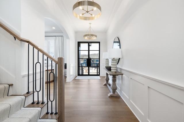 entrance foyer featuring a wainscoted wall, arched walkways, dark wood-style flooring, stairs, and a notable chandelier