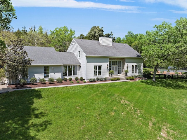 back of house featuring a chimney, roof with shingles, a yard, and fence