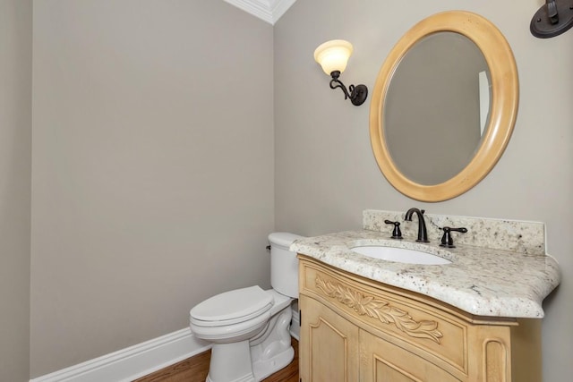 half bath featuring vanity, wood finished floors, baseboards, crown molding, and toilet