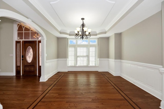 unfurnished dining area with a chandelier, a tray ceiling, wainscoting, wood finished floors, and arched walkways