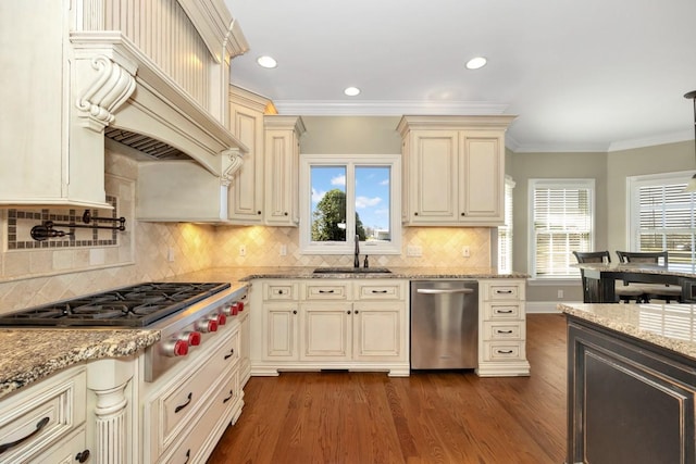 kitchen with dark wood-type flooring, cream cabinetry, a sink, appliances with stainless steel finishes, and crown molding