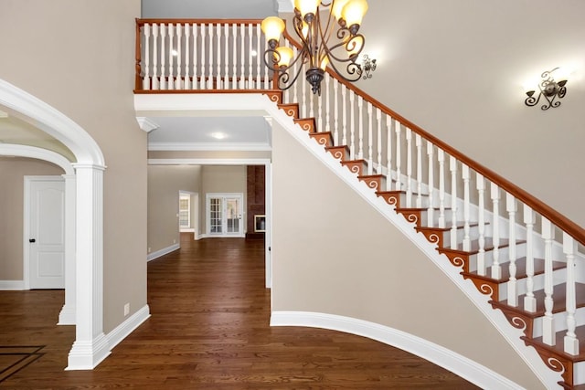 staircase featuring baseboards, a high ceiling, an inviting chandelier, wood finished floors, and ornate columns