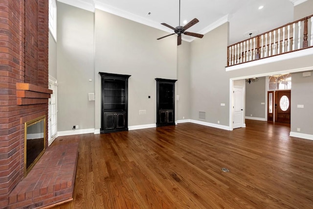 unfurnished living room featuring wood finished floors, crown molding, baseboards, a brick fireplace, and ceiling fan