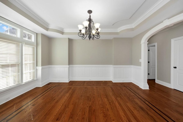 empty room featuring a wainscoted wall, arched walkways, a notable chandelier, and wood finished floors