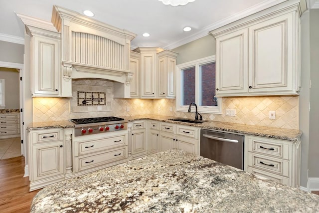 kitchen featuring light stone counters, a sink, cream cabinetry, appliances with stainless steel finishes, and crown molding