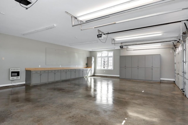 garage featuring heating unit, a garage door opener, and baseboards