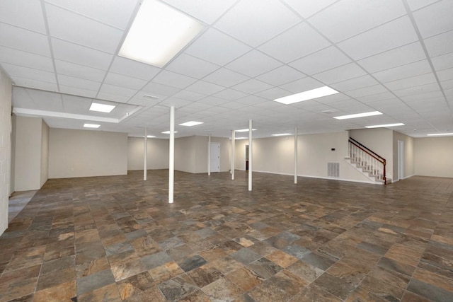 finished basement with visible vents, stone finish flooring, stairs, and a paneled ceiling