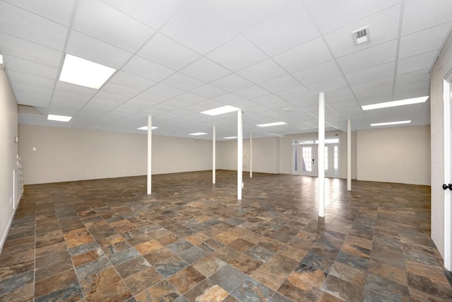 below grade area featuring a drop ceiling, visible vents, and stone finish floor