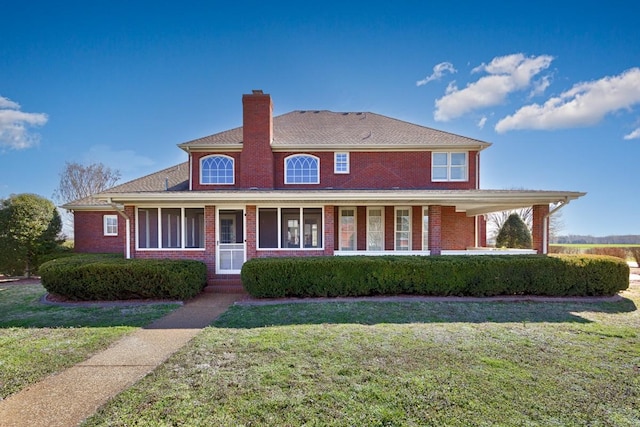 view of front of house featuring brick siding, a chimney, covered porch, and a front yard