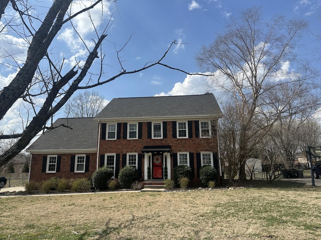 colonial house featuring a front yard, fence, and brick siding