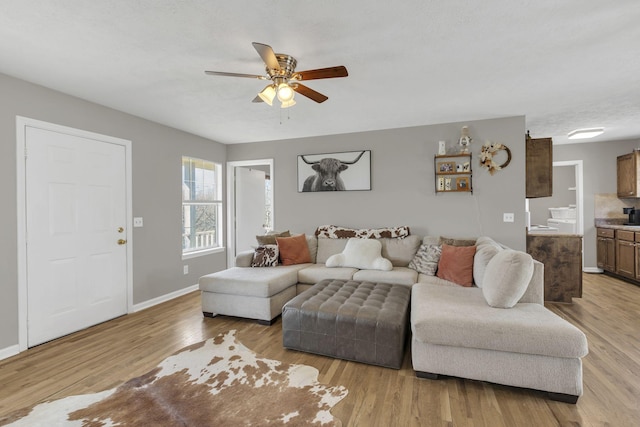 living room featuring light wood-style flooring, a ceiling fan, and baseboards