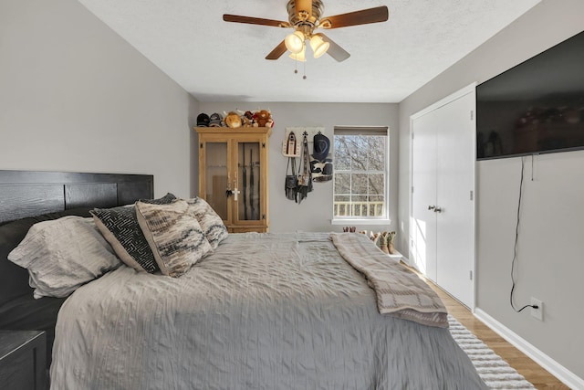 bedroom featuring a ceiling fan, wood finished floors, baseboards, and a textured ceiling