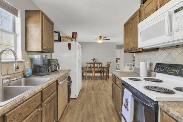 kitchen with white appliances, brown cabinetry, light wood finished floors, a sink, and tasteful backsplash