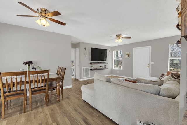 living room featuring ceiling fan, visible vents, baseboards, and wood finished floors