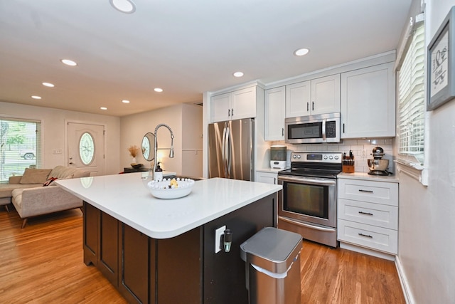 kitchen featuring light wood finished floors, stainless steel appliances, light countertops, white cabinets, and backsplash