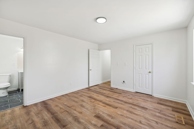 unfurnished bedroom with ensuite bath, wood finished floors, visible vents, and baseboards