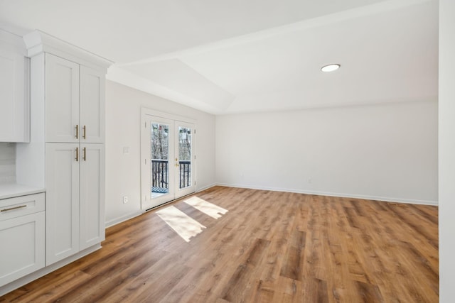 interior space featuring light wood-style flooring, a tray ceiling, french doors, baseboards, and vaulted ceiling