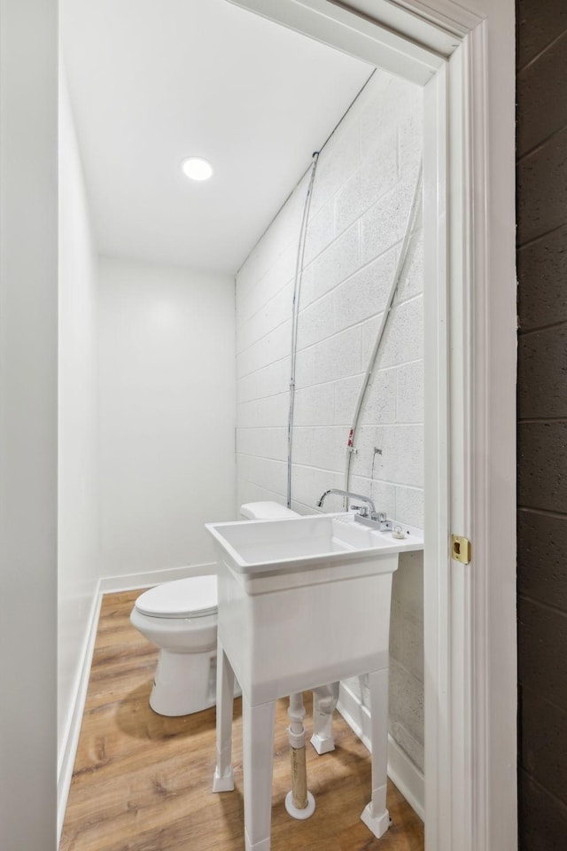 bathroom with baseboards, toilet, wood finished floors, and concrete block wall